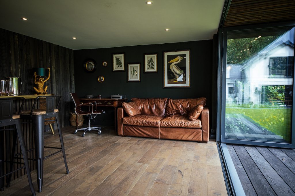 Office desk next to a leather sofa inside a garden room