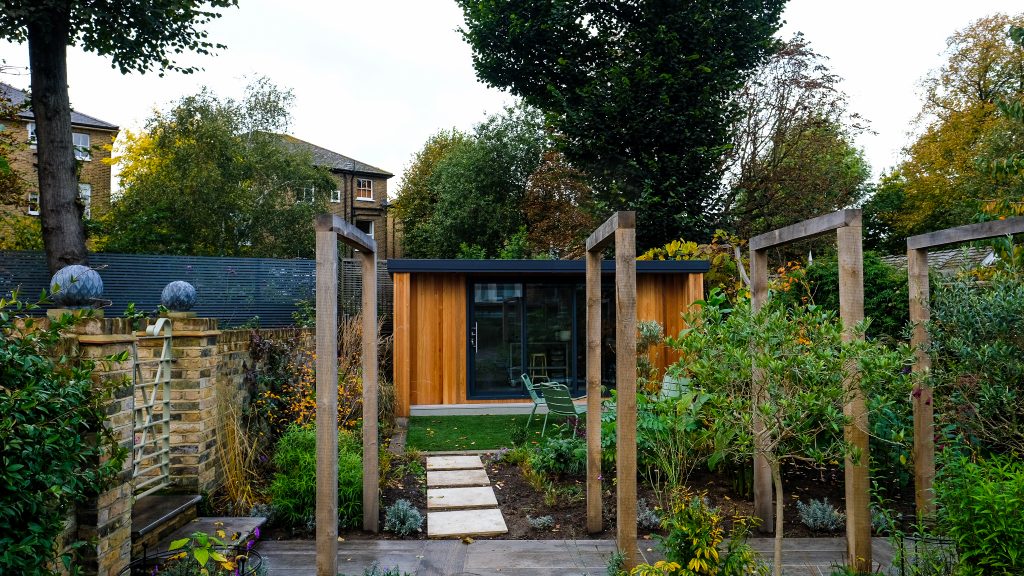 Small wooden building in the middle of a green garden with plants